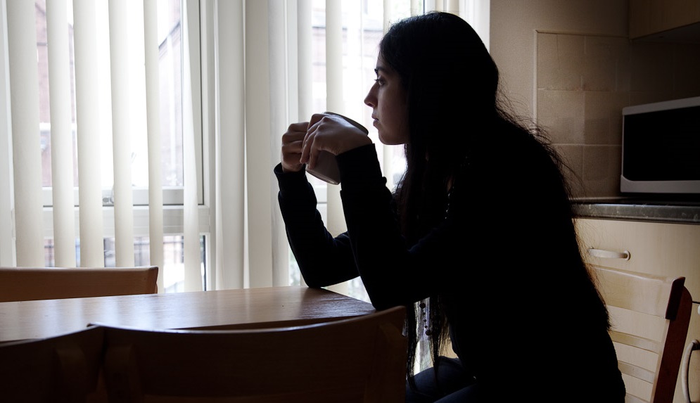 A woman sat at a table holding a mug looking out of the window.